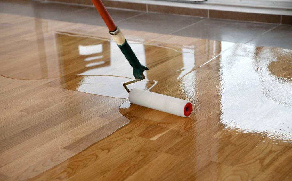 The image shows a professional applying a protective sealant to a wooden floor, offering floor sealing services to enhance durability and shine.