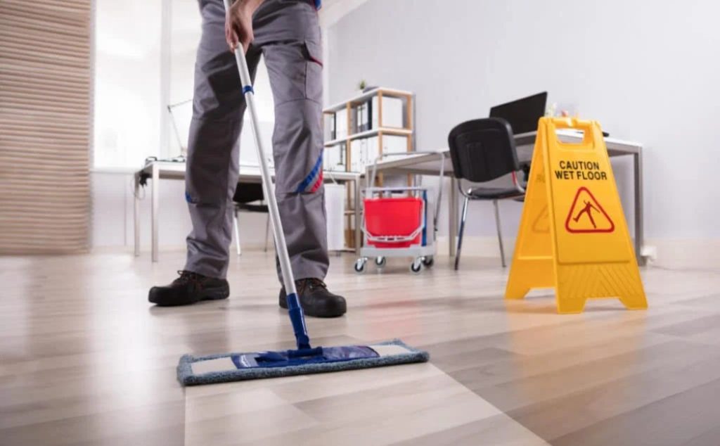 The image shows a professional cleaning a wooden floor with a mop, providing expert floor cleaning services to maintain a spotless environment.