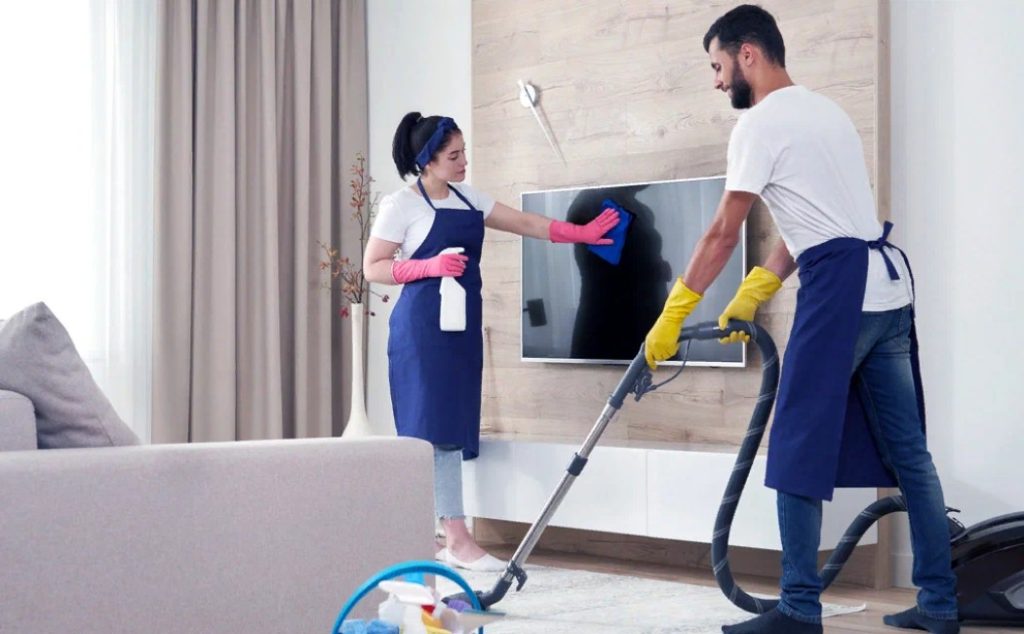 The image shows a couple performing detailed cleaning tasks in a living room, highlighting the need for Residential Specialty Cleaning Services for thorough home upkeep.