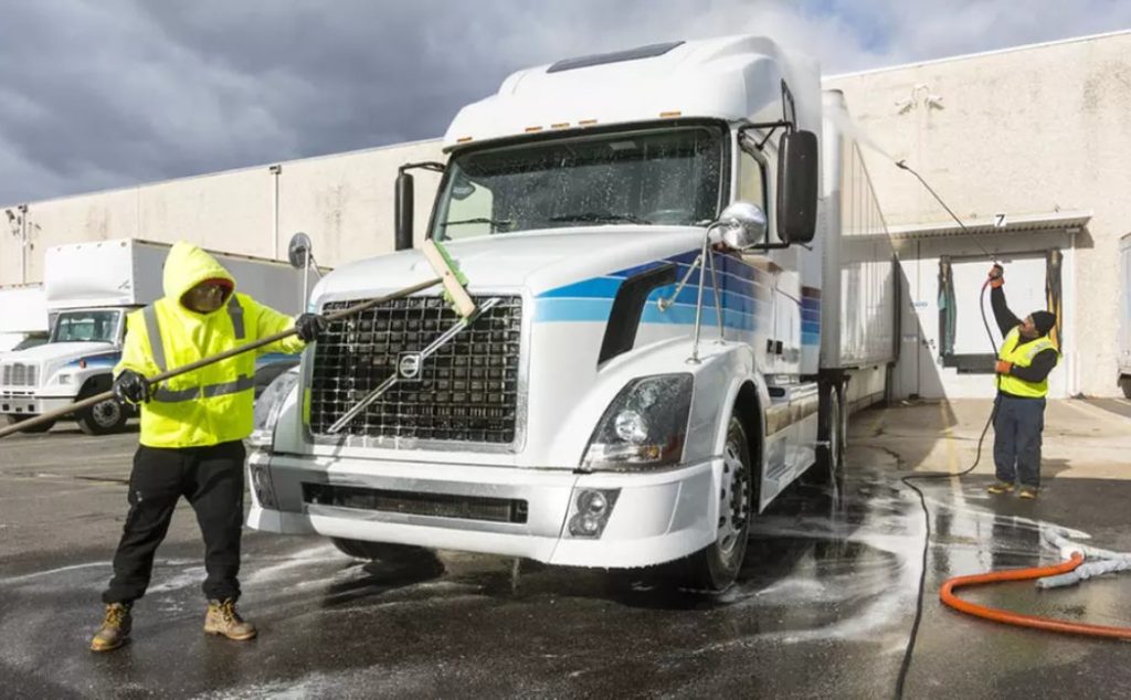 Two workers are washing a large truck with high-pressure water, demonstrating the thorough approach of Specialty RV Cleaning Services for large vehicles like trucks and RVs.