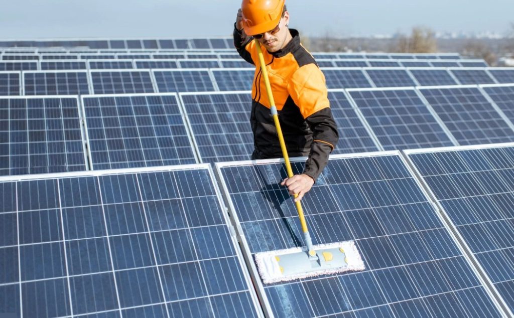 A worker in protective gear carefully cleans solar panels, demonstrating the precision and care involved in Specialty Solar Panel Cleaning Services to maintain optimal performance.