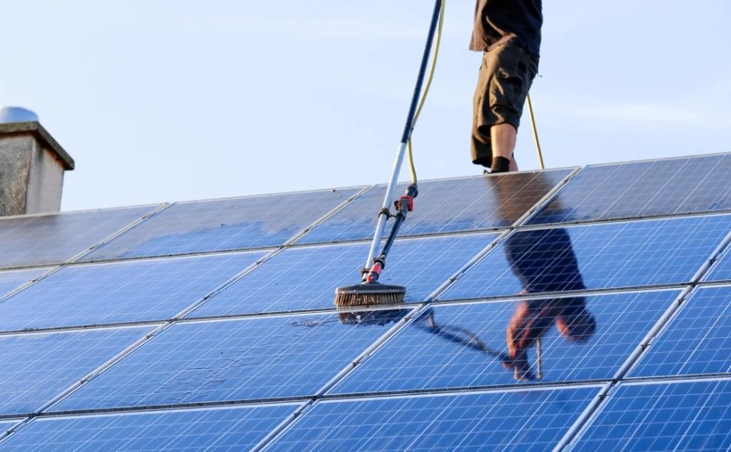 A worker uses professional equipment to clean rooftop solar panels under clear skies, showcasing Specialty Solar Panel Cleaning Services in action.