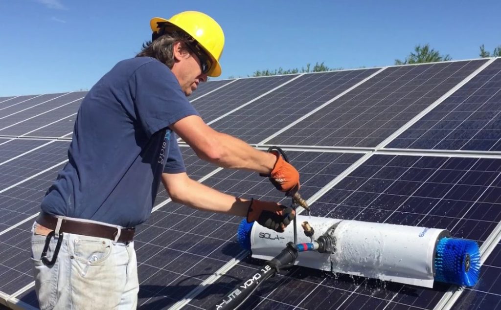 A technician in safety gear operates advanced equipment to clean solar panels, demonstrating efficient Specialty Solar Panel Cleaning Services under sunny conditions.