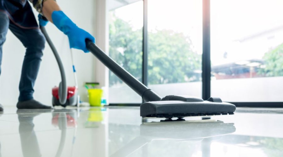 A professional cleaner in gloves is vacuuming the floor of a bright room, showcasing the effectiveness of Professional Cleaning Services.