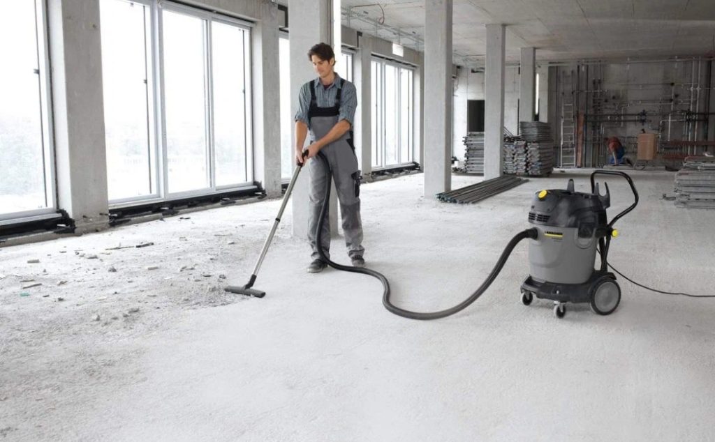 A worker is using a vacuum cleaner to remove construction debris, offering commercial after construction cleaning services in a newly built space.