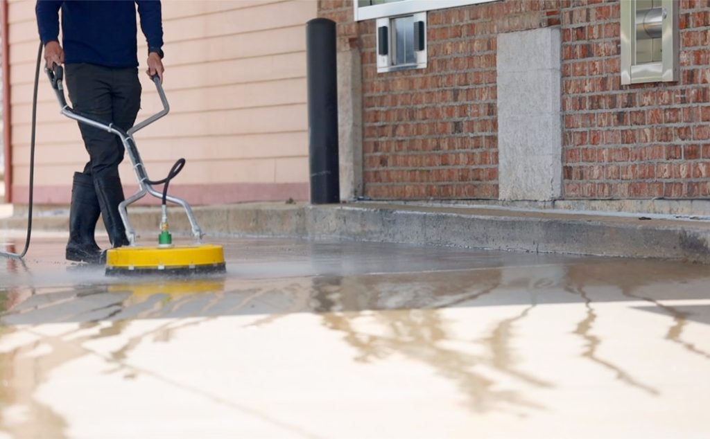 A professional using a commercial power washer to clean a concrete surface, showcasing the effectiveness of Commercial Power Washing Services for businesses and properties.